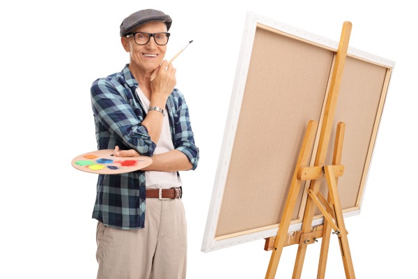 Senior,Artist,Holding,A,Paintbrush,And,Posing,Next,To,A